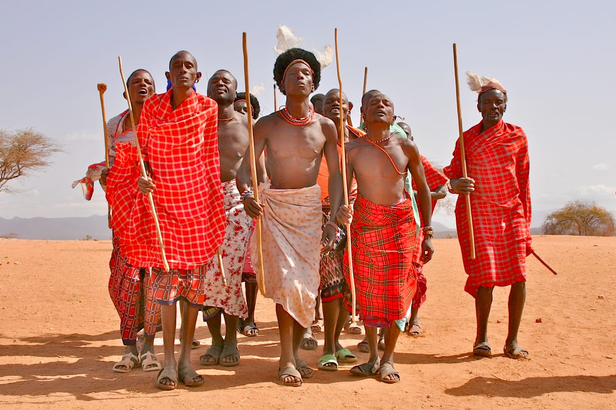 A tribe of topless tribal males approach dressed in red with eyes closed in ceremony.
