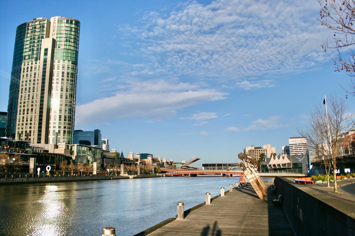 A wide river flanked by concrete walkways, sculptures and a red bridge spanning the water.